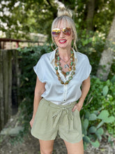 Woman wearing a white shirt and green checkered shorts with sunglasses outdoors.