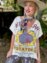 Woman wearing a vintage-style potato farmer t-shirt with a colorful scarf and wide-brimmed hat.
