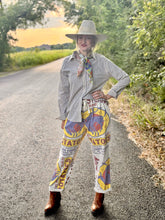 Person wearing colorful patterned pants and a hat on a road with greenery.