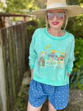 Woman wearing a light blue sweatshirt with western characters and blue shorts outdoors.
