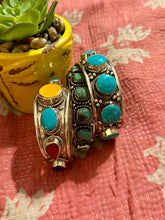 Decorative bracelets with turquoise stones on a pink textured surface with a plant in the background.