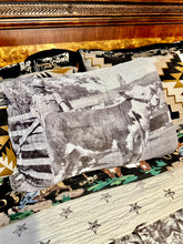 A western-themed bedding set featuring a printed pillow with a black and white cow photograph, a patterned quilt with star motifs, and matching patterned pillows in front of a dark wood headboard.