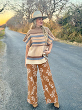 Woman in a striped sweater and floral pants standing on a road with trees in the background