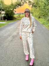 Person wearing a western print outfit with pink high tops standing on a road during sunset.