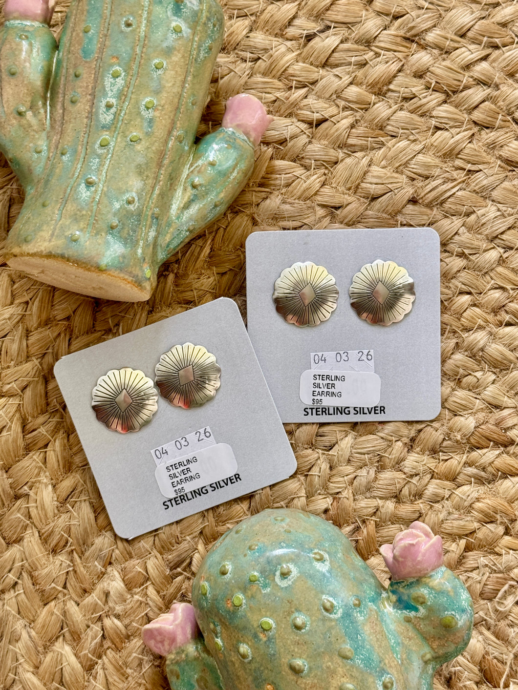 silver earrings on cards with 'Sterling Silver' label, surrounded by decorative cacti on a woven surface.