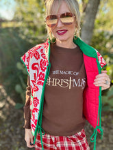 Woman wearing a 'The Magic of Christmas' shirt with a red and green vest outdoors.