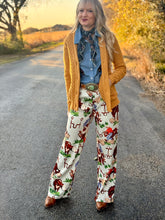 Person wearing a mustard yellow cardigan, blue shirt, and patterned pants standing on a road with autumn scenery.