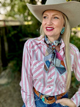 Woman wearing a pink and white striped shirt, cowboy hat, and colorful scarf outdoors.