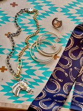 Jewelry set with a horse  necklacea, a horseshoe ring and earrings on a patterned surface