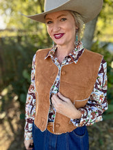 Woman wearing a cowboy hat, brown vest, and patterned shirt outdoors.