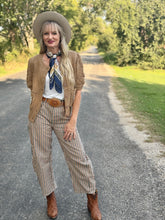 Woman in a stylish outfit with a hat, cardigan, and striped pants standing on a road.