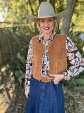 Person wearing a cowboy hat, brown vest, patterned shirt, and blue jean skirt outdoors.