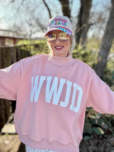 Person wearing a pink sweatshirt with 'WWJD' text and a colorful cap outdoors.