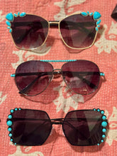 Three pairs of sunglasses with turquoise embellishments on a floral fabric background