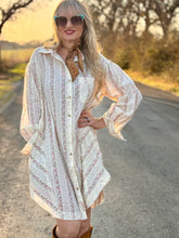 Woman in a white patterned dress standing on a road with trees in the background