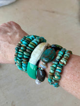 Wrist wearing multiple turquoise beaded bracelets on a neutral background