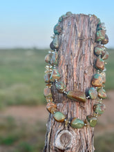 Necklace with green and brown stones on a wooden post against a natural background
