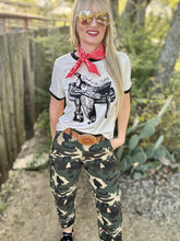 Woman wearing a graphic t-shirt, camouflage pants, and a red bandana outdoors.