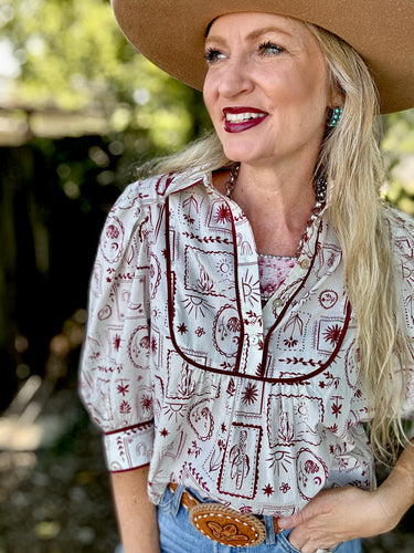 Woman wearing a patterned blouse and cowboy hat outdoors
