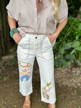 Person wearing a striped shirt and white pants with colorful embroidery, standing outdoors.