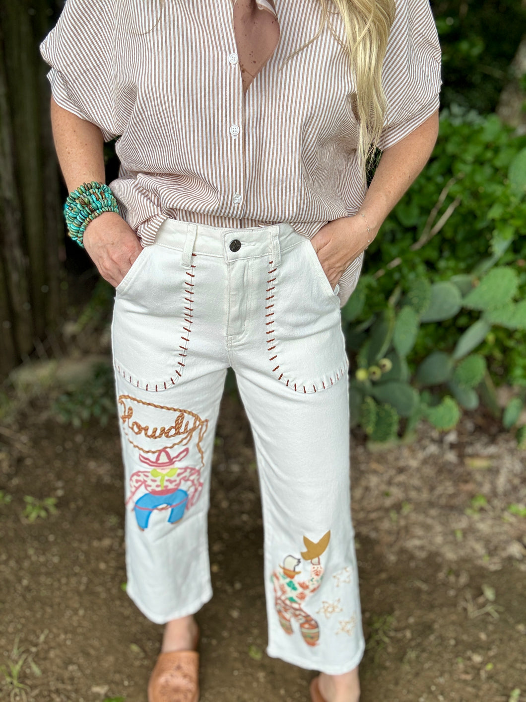 Person wearing a striped shirt and white pants with colorful embroidery, standing outdoors.