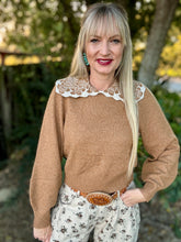 Woman wearing a brown sweater with lace collar and floral pants outdoors.