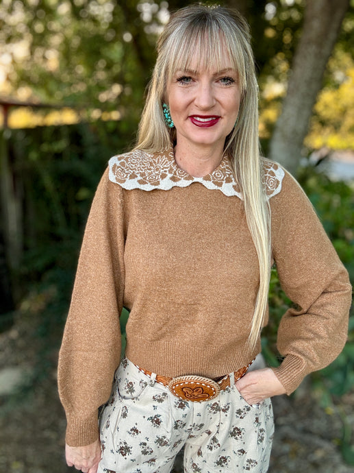 Woman wearing a brown sweater with lace collar and floral pants outdoors.