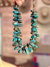 Turquoise stone necklace held by a hand with a blurred background