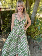 Woman wearing a green floral dress standing outdoors with trees in the background