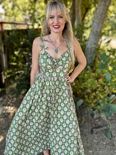 Woman wearing a green floral dress standing outdoors with trees in the background