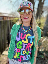 Woman wearing a colorful 'Just a Girl Who Loves Jesus' shirt with a green cardigan and sunglasses.