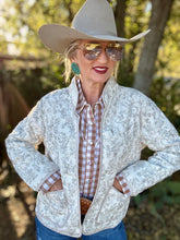 Woman wearing a white horse print  jacket, plaid shirt, and cowboy hat outdoors.