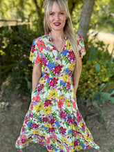 Woman wearing a colorful floral dress standing outdoors with greenery in the background