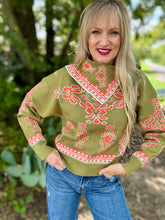 Woman wearing a green sweater with coral patterns and blue jeans outdoors.