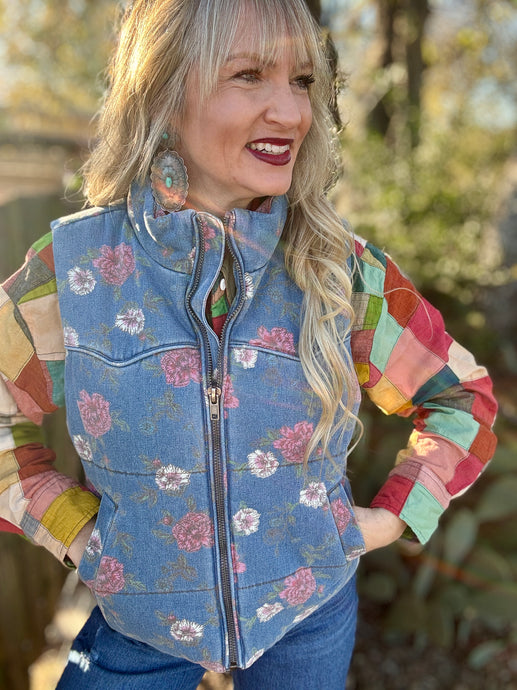 Woman wearing a colorful patchwork jacket with a floral-patterned vest outdoors.
