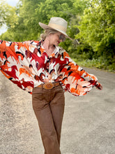 Person wearing a colorful patterned shirt and brown pants on a road with greenery in the background