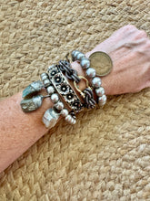 Wrist wearing multiple silver bracelets on a woven surface