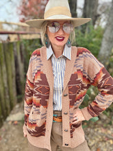Person wearing a patterned cardigan, sunglasses, and hat outdoors.