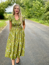 Woman in a green floral dress standing on a road with trees in the background