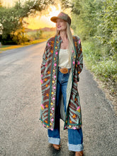 Woman wearing a colorful patterned cardigan on a road with nature in the background