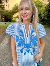 Woman wearing a blue and white striped dress with floral patterns outdoors.