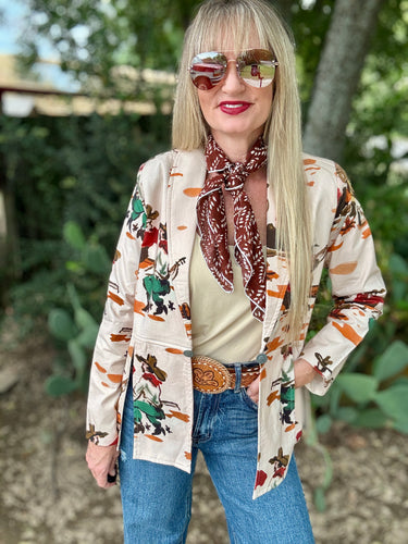Woman wearing a patterned blazer, scarf, and jeans with sunglasses outdoors.