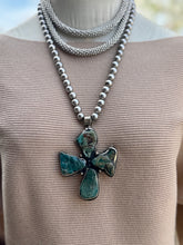 Necklace with a cross pendant on a mannequin wearing a beige sweater.