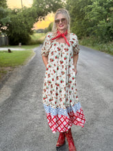 Woman in a floral dress with a red scarf and red boots standing on a road.