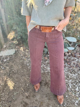 Person wearing a green patterned shirt and brown flared pants in a natural setting.