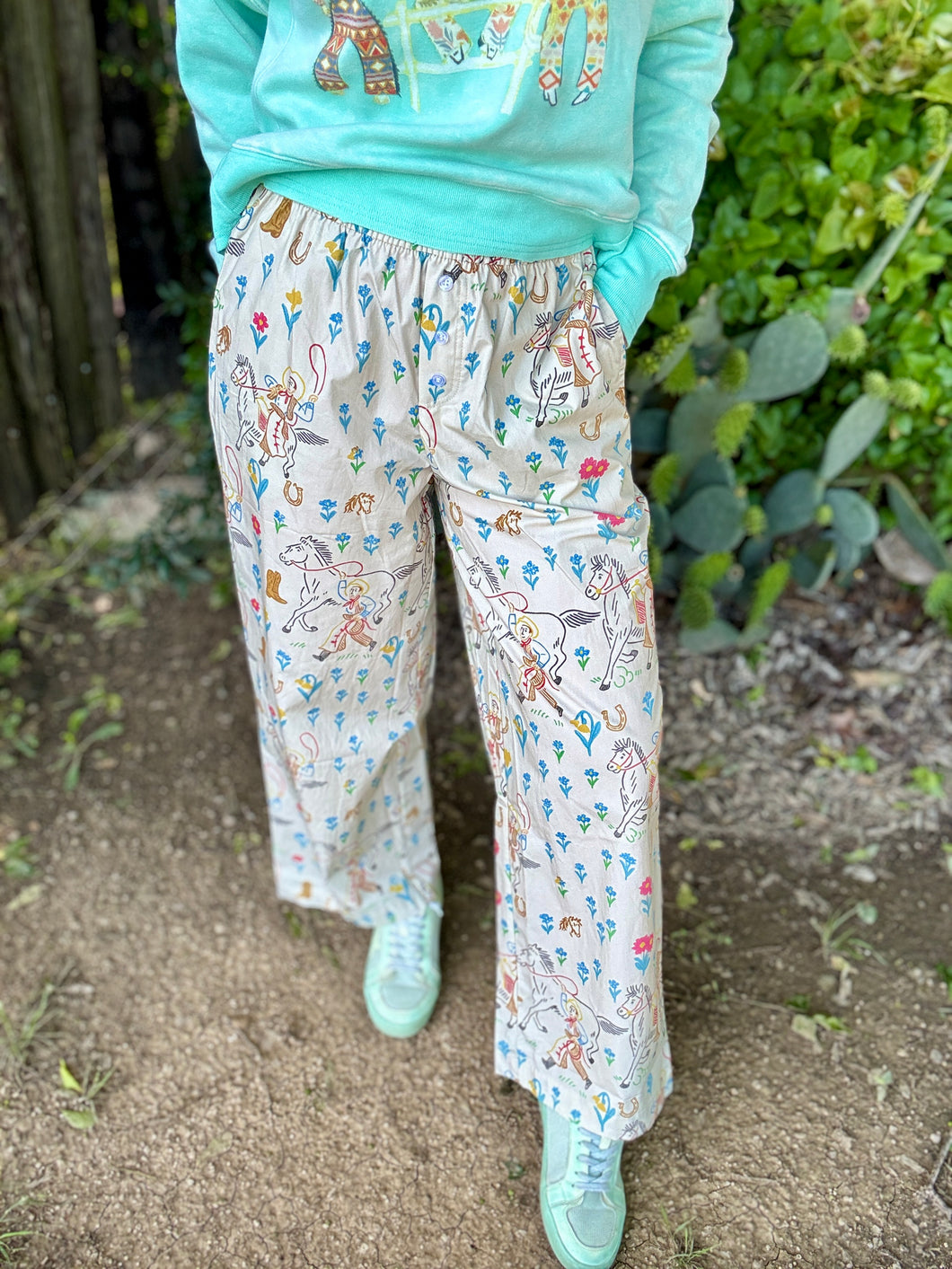 wearing a light blue sweatshirt and patterned pants standing outdoors.