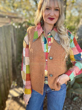 Woman wearing a colorful plaid shirt, brown vest, and blue jeans outdoors.