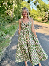 Woman in a green floral dress standing on a path with trees in the background