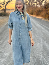 Woman wearing a denim dress standing on a rural road with trees and sunset in the background