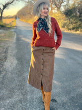 Woman in a red sweater and brown skirt standing on a road with a scenic background